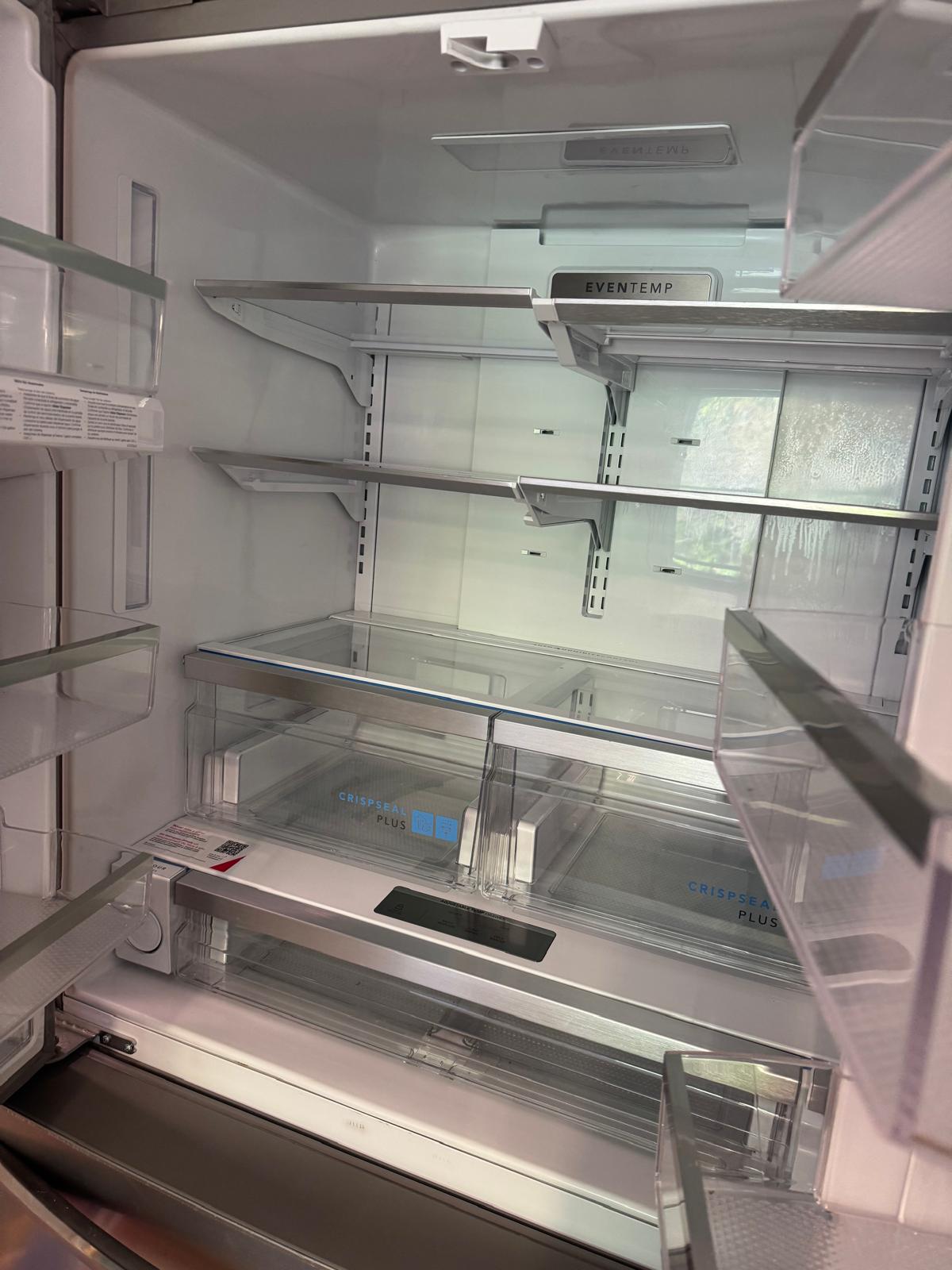 Empty French-door refrigerator with every glass shelf, door bin and crisper drawer wiped clean and bare